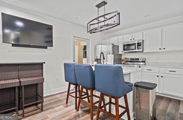 kitchen featuring appliances with stainless steel finishes, a kitchen island, hardwood / wood-style flooring, decorative light fixtures, and white cabinetry