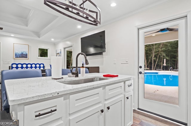 kitchen featuring white cabinetry, sink, light stone counters, an island with sink, and ornamental molding