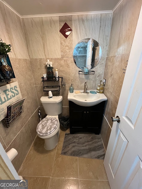 bathroom with tile walls, vanity, toilet, and ornamental molding