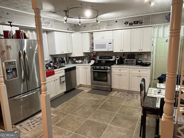 kitchen with dark tile patterned floors, a textured ceiling, white cabinets, decorative backsplash, and appliances with stainless steel finishes