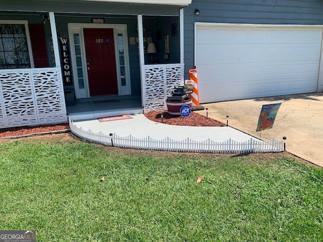 view of exterior entry with a lawn, a garage, and covered porch