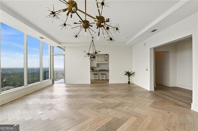 unfurnished living room featuring an inviting chandelier, light parquet flooring, and a wealth of natural light