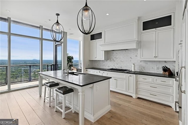 kitchen featuring white cabinets, a center island with sink, hanging light fixtures, and sink