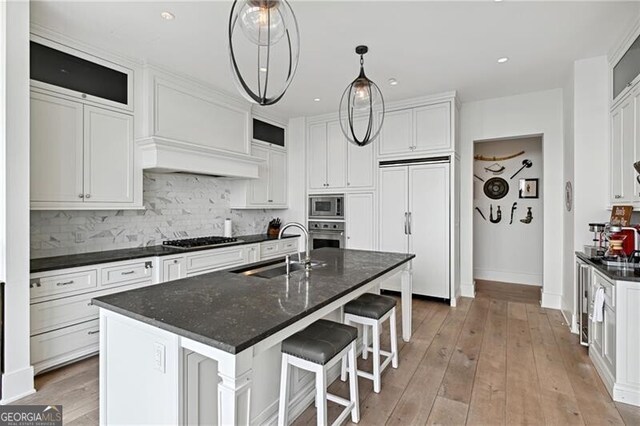 kitchen with white cabinets, built in appliances, a center island with sink, and sink