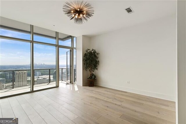 spare room with an inviting chandelier, light hardwood / wood-style floors, a wall of windows, and plenty of natural light