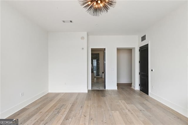 unfurnished room with an inviting chandelier and light hardwood / wood-style floors