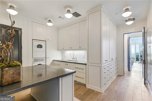 kitchen with light wood-type flooring, stacked washer and dryer, and white cabinetry