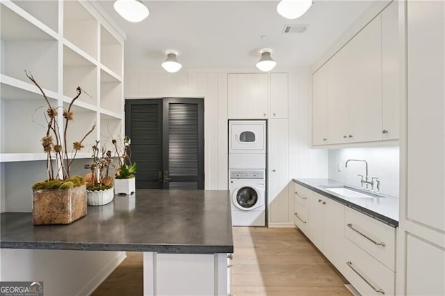 kitchen with white cabinetry, light hardwood / wood-style floors, stacked washer / dryer, and sink