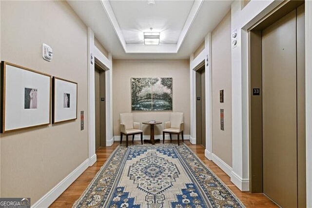 corridor with wood-type flooring, a raised ceiling, and elevator