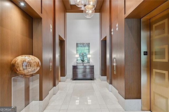 hallway featuring light tile patterned flooring, wooden walls, a towering ceiling, and a notable chandelier