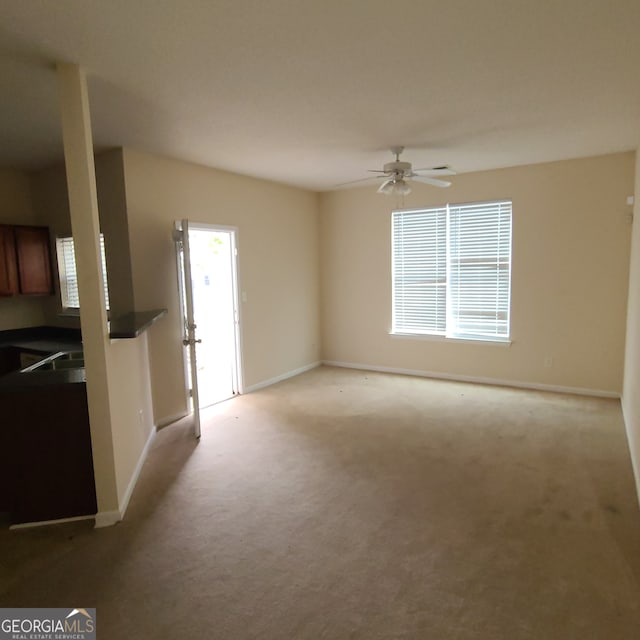 unfurnished living room featuring sink, light carpet, and ceiling fan