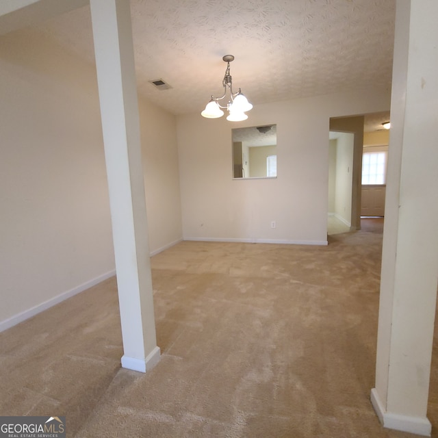 carpeted spare room featuring a chandelier and a textured ceiling