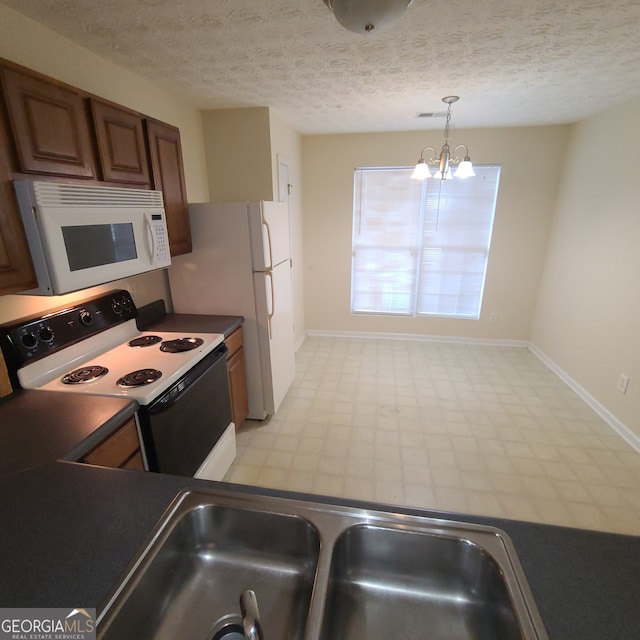 kitchen with a textured ceiling, a notable chandelier, hanging light fixtures, and white appliances