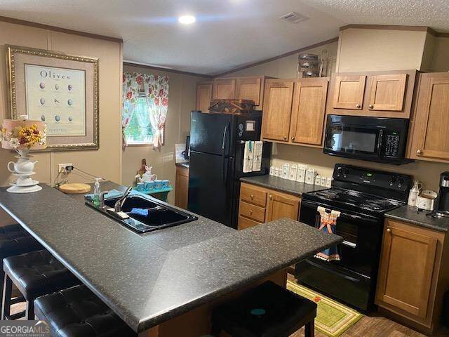 kitchen featuring lofted ceiling, ornamental molding, sink, black appliances, and a kitchen breakfast bar