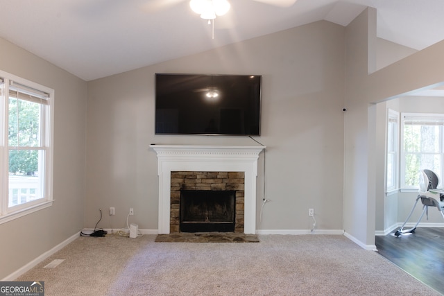 unfurnished living room featuring lofted ceiling, a stone fireplace, carpet flooring, and plenty of natural light