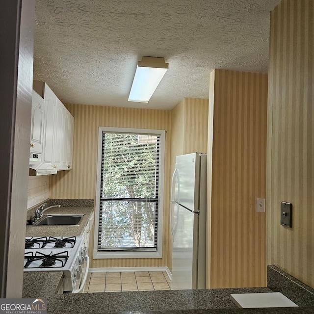 kitchen with light tile patterned flooring, white cabinetry, white gas range oven, refrigerator, and sink