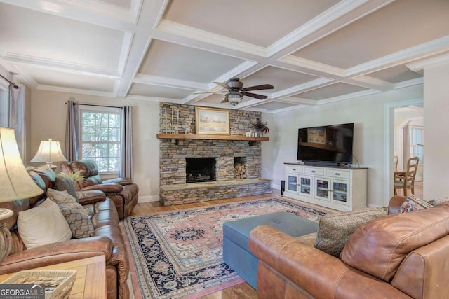 living area with beam ceiling, ceiling fan, a stone fireplace, and wood finished floors