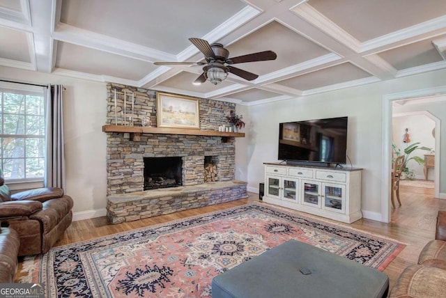 living room with ceiling fan, a stone fireplace, coffered ceiling, baseboards, and light wood finished floors