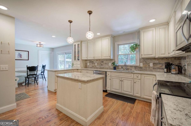 kitchen featuring glass insert cabinets, decorative light fixtures, a center island, light stone countertops, and stainless steel appliances