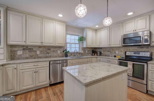 kitchen with a center island, pendant lighting, light wood finished floors, stainless steel appliances, and a sink