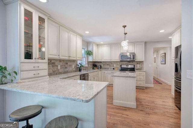 kitchen featuring a breakfast bar, hanging light fixtures, appliances with stainless steel finishes, glass insert cabinets, and a peninsula