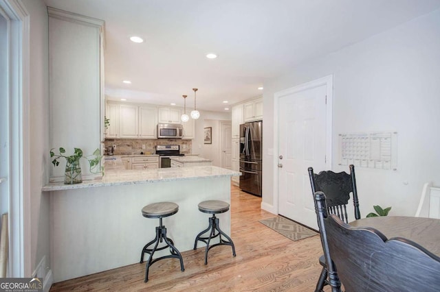 kitchen featuring stainless steel appliances, hanging light fixtures, a peninsula, and white cabinets