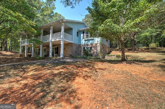 view of front of house featuring stone siding, a balcony, and a front lawn