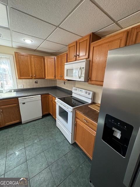 kitchen with tasteful backsplash, dark countertops, white appliances, and brown cabinets