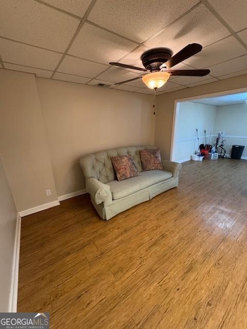 unfurnished living room featuring a ceiling fan, a paneled ceiling, baseboards, and wood finished floors