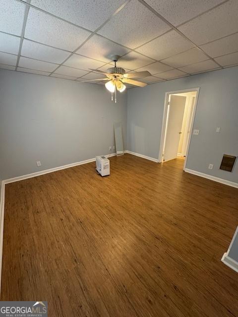 unfurnished room with a ceiling fan, wood finished floors, a paneled ceiling, and baseboards