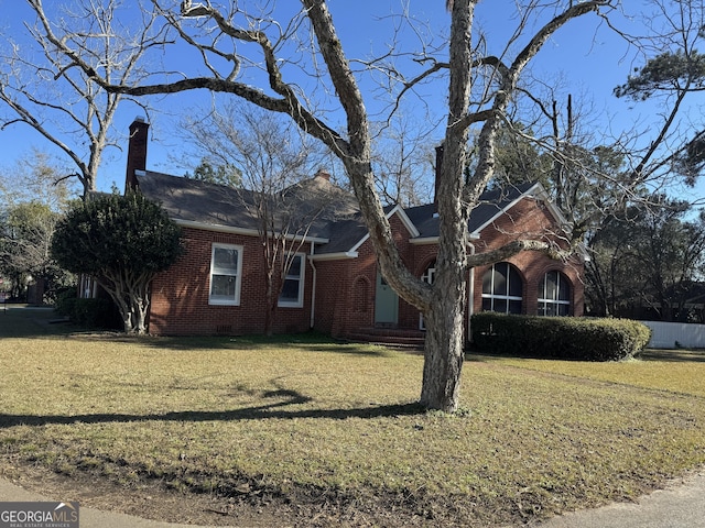 view of front facade with a chimney, a front yard, and brick siding
