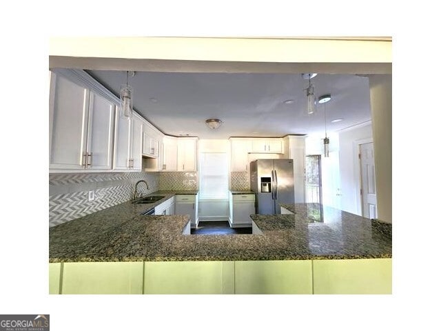 kitchen with white cabinetry, hanging light fixtures, stainless steel fridge, kitchen peninsula, and decorative backsplash