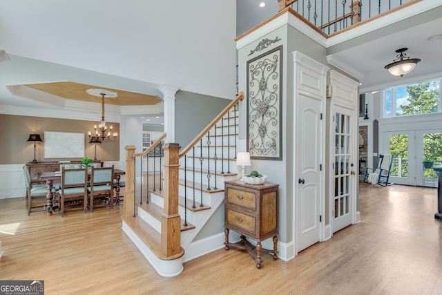 staircase featuring a towering ceiling, wood-type flooring, a chandelier, ornate columns, and french doors