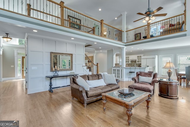 living room featuring ornamental molding, ornate columns, a high ceiling, ceiling fan, and light hardwood / wood-style flooring