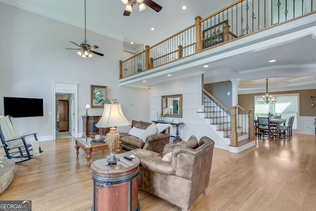 living room featuring decorative columns, a towering ceiling, ceiling fan with notable chandelier, and ornamental molding