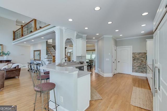 kitchen with white cabinets, kitchen peninsula, a breakfast bar area, light stone countertops, and light wood-type flooring