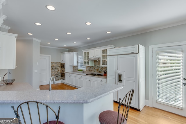 kitchen with a kitchen bar, built in appliances, white cabinetry, and kitchen peninsula