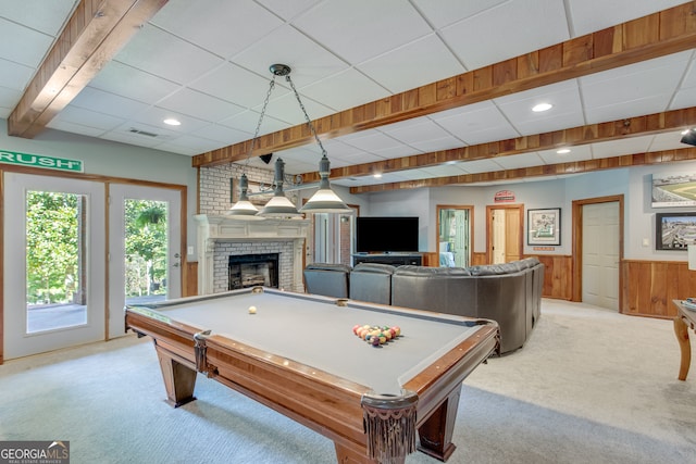 recreation room with beamed ceiling, a brick fireplace, light colored carpet, wooden walls, and billiards