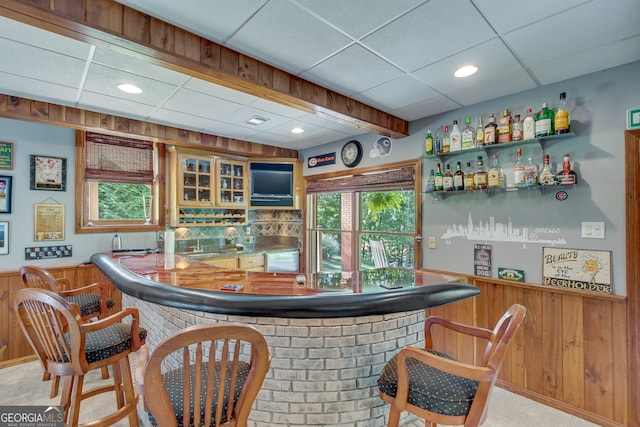 bar with wood walls, backsplash, a drop ceiling, and carpet floors