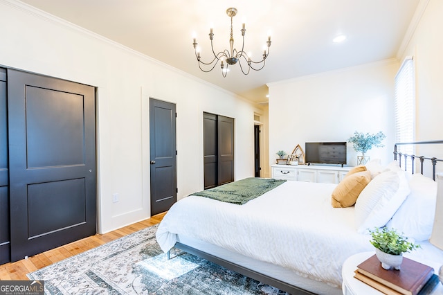 bedroom with multiple closets, light hardwood / wood-style flooring, a chandelier, and ornamental molding