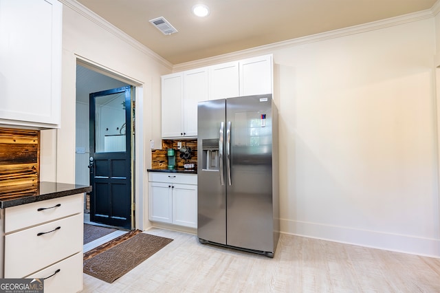 kitchen with stainless steel refrigerator with ice dispenser, decorative backsplash, white cabinets, dark stone counters, and ornamental molding