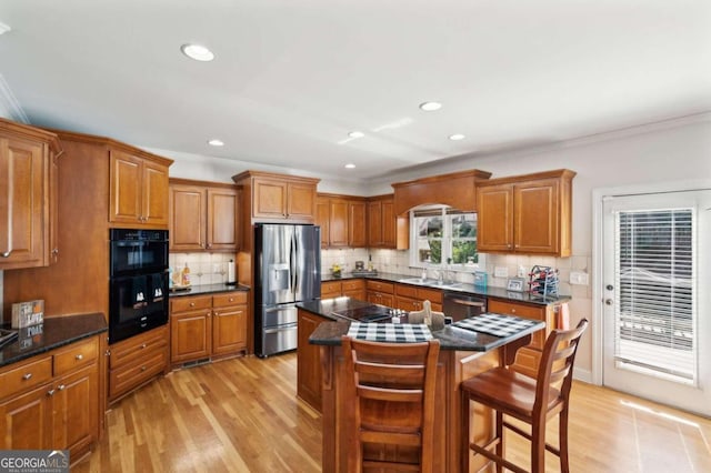 kitchen with appliances with stainless steel finishes, decorative backsplash, a kitchen island, a kitchen bar, and light hardwood / wood-style flooring