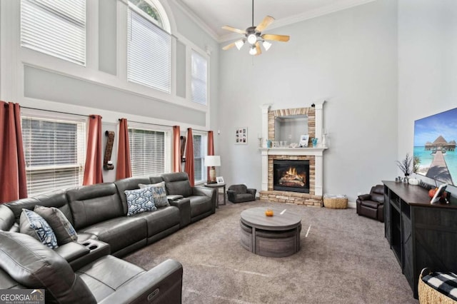 living room with carpet floors, a stone fireplace, crown molding, a high ceiling, and ceiling fan