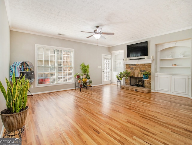 living room with light wood-type flooring, a textured ceiling, a fireplace, ceiling fan, and built in features