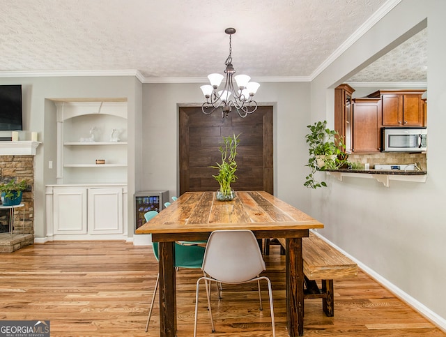 dining area with built in shelves, a textured ceiling, a notable chandelier, crown molding, and light hardwood / wood-style floors