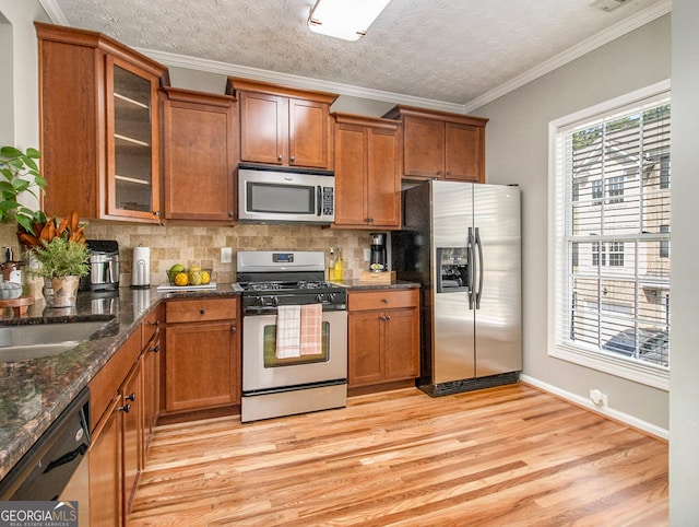 kitchen featuring ornamental molding, backsplash, stainless steel appliances, dark stone countertops, and light wood-type flooring