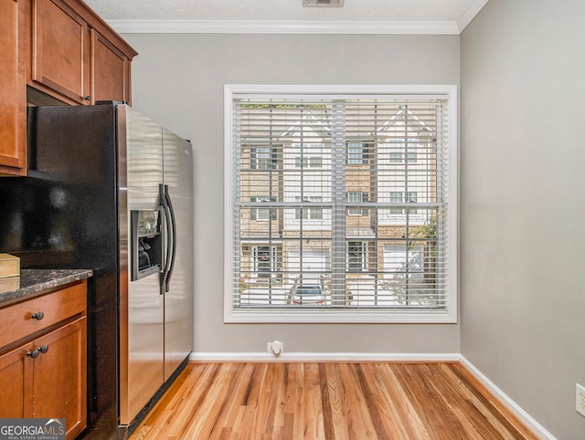 kitchen featuring stainless steel fridge, light hardwood / wood-style floors, ornamental molding, and dark stone countertops