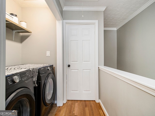 washroom featuring a textured ceiling, crown molding, light hardwood / wood-style floors, and washing machine and clothes dryer