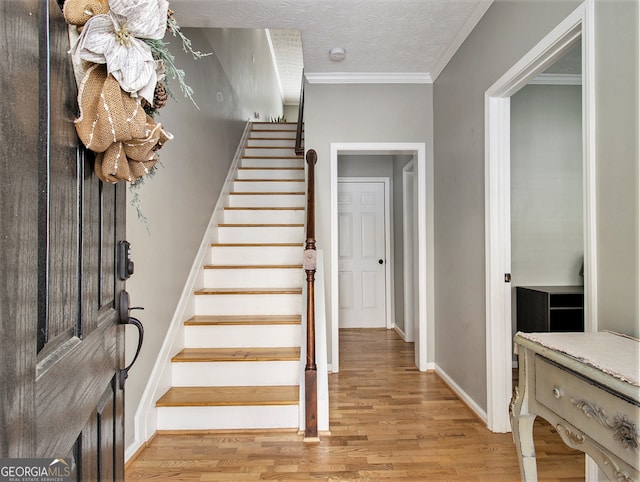 stairs with ornamental molding, a textured ceiling, and hardwood / wood-style floors