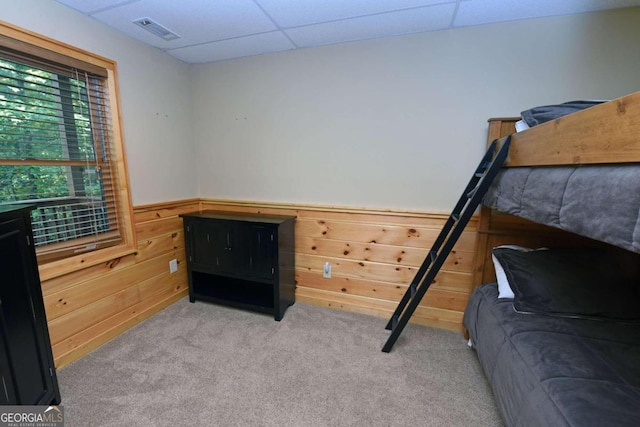 carpeted bedroom featuring a drop ceiling and wood walls